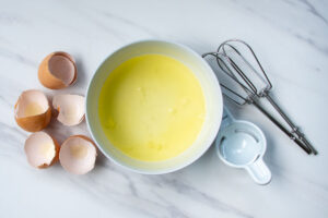 egg shells, egg whites in a bowl, egg separator, mixer beaters