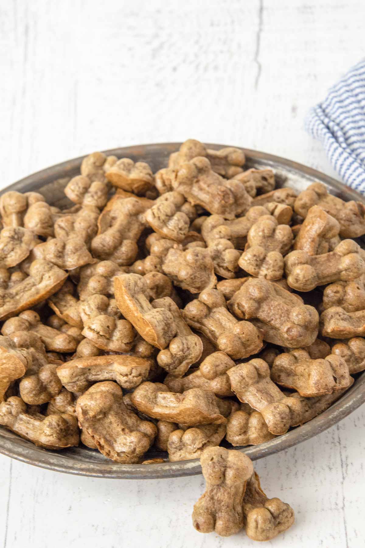 A bowl of homemade bone-shaped liver dog treats on a wood surface.