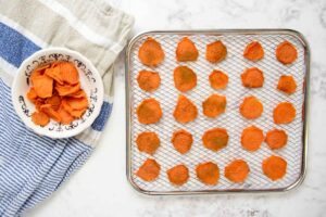 dehydrated sweet potato slices on a dehydrator rack and in a bowl.