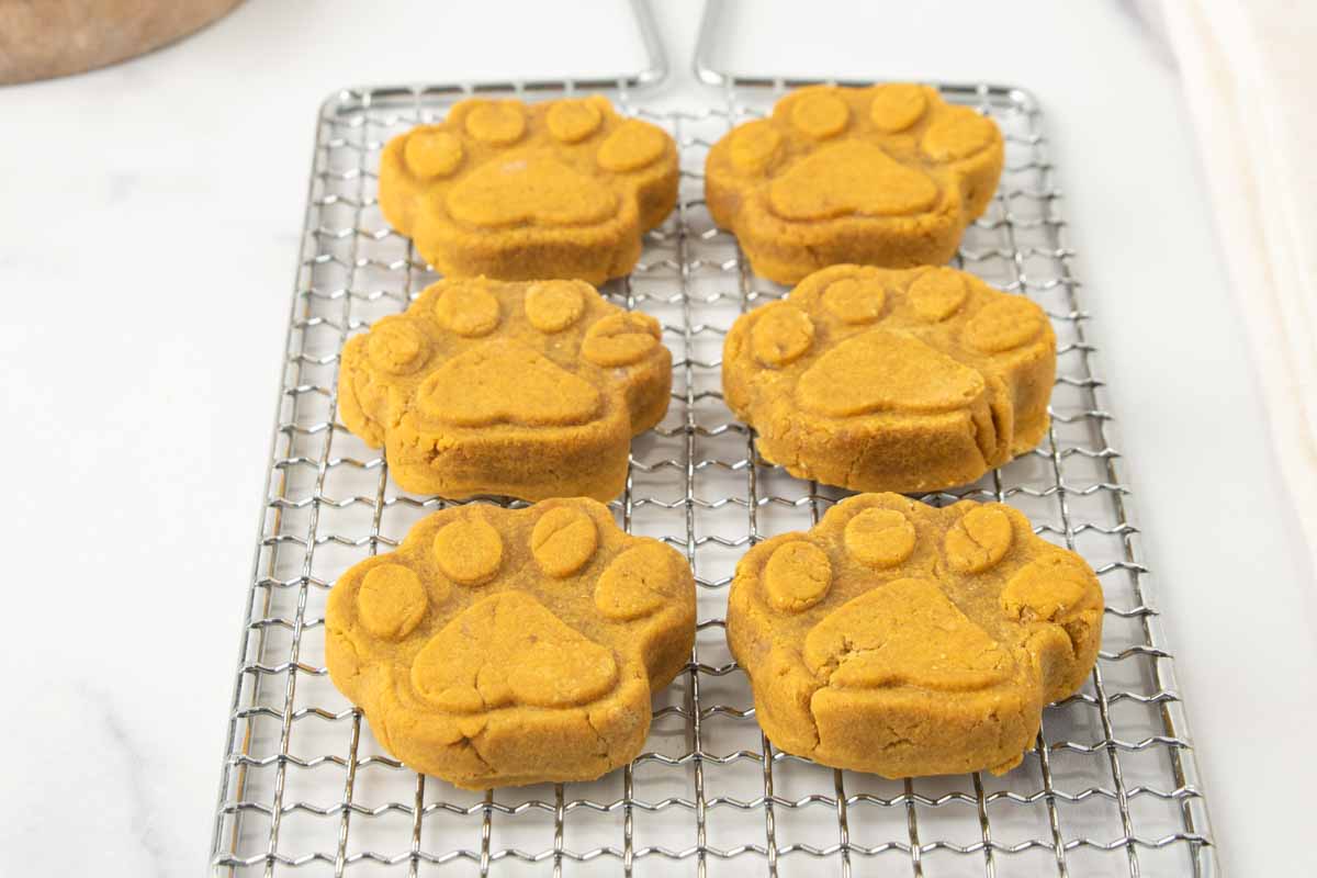 six homemade paw-shaped pumpkin dog biscuits on a wire rack.