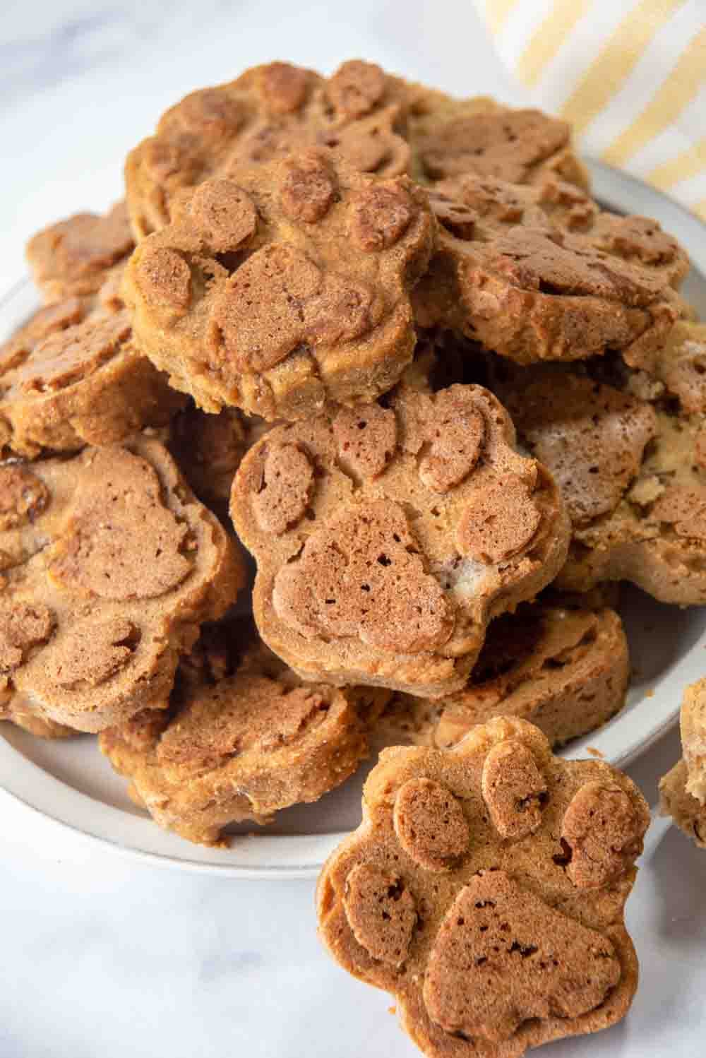 Paw-shaped baked dog treats made with applesauce piled on a plate.