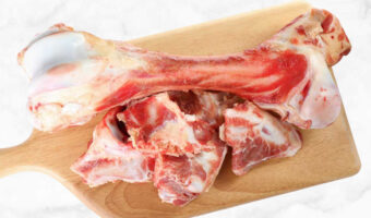 Assorted raw lamb bones on a wood cutting board.