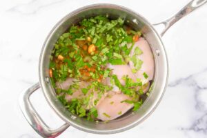 Raw chicken, vegetables, parsley, and water in a pot.