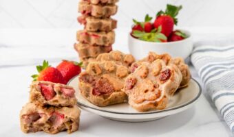 Homemade strawberry dog treats on a plate and stacked and a bowl of strawberries.
