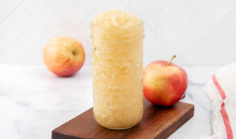 Homemade applesauce for dogs in a glass jar and two apples.