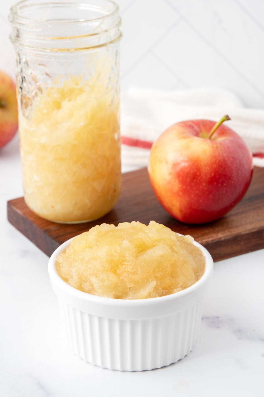 Homemade applesauce for dogs in a ramekin and glass jar and an apple.