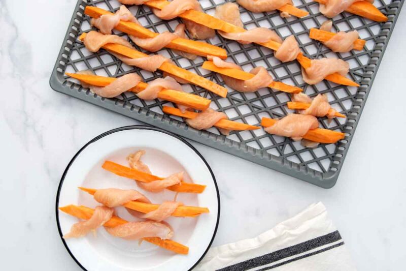 Chicken wrapped sweet potato strips on a plate and dehydrator rack.