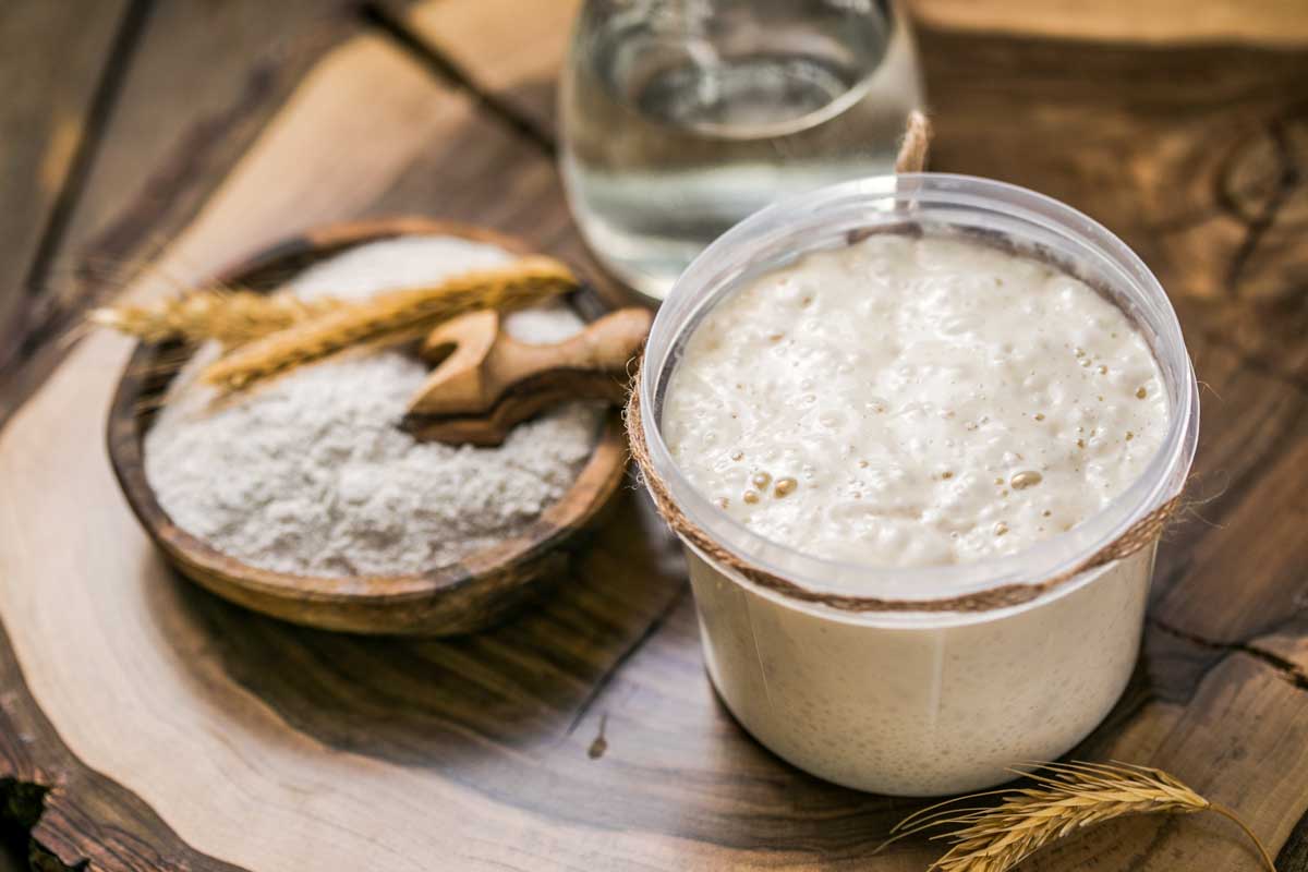 Sourdough starter in a jar and a bowl of flour.