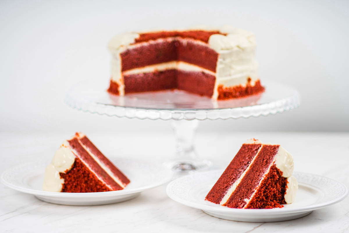 Red velvet cake on a cake stand and slices on a plates.