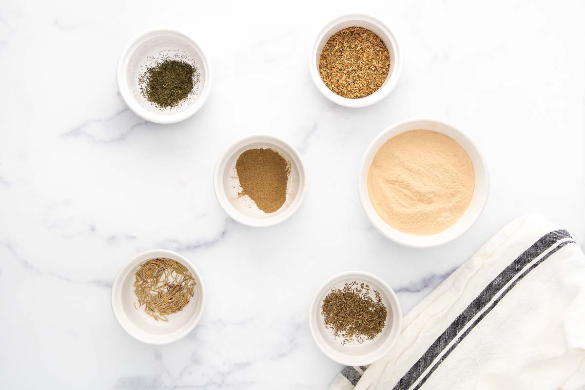 Homemade brewers yeast herb blend ingredients in bowls on a marble surface.