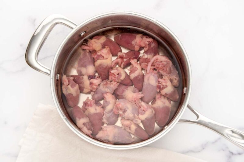 Raw chicken hearts and water in a pan.