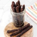 Homemade venison jerky for dogs in a glass jar and on a wood board.