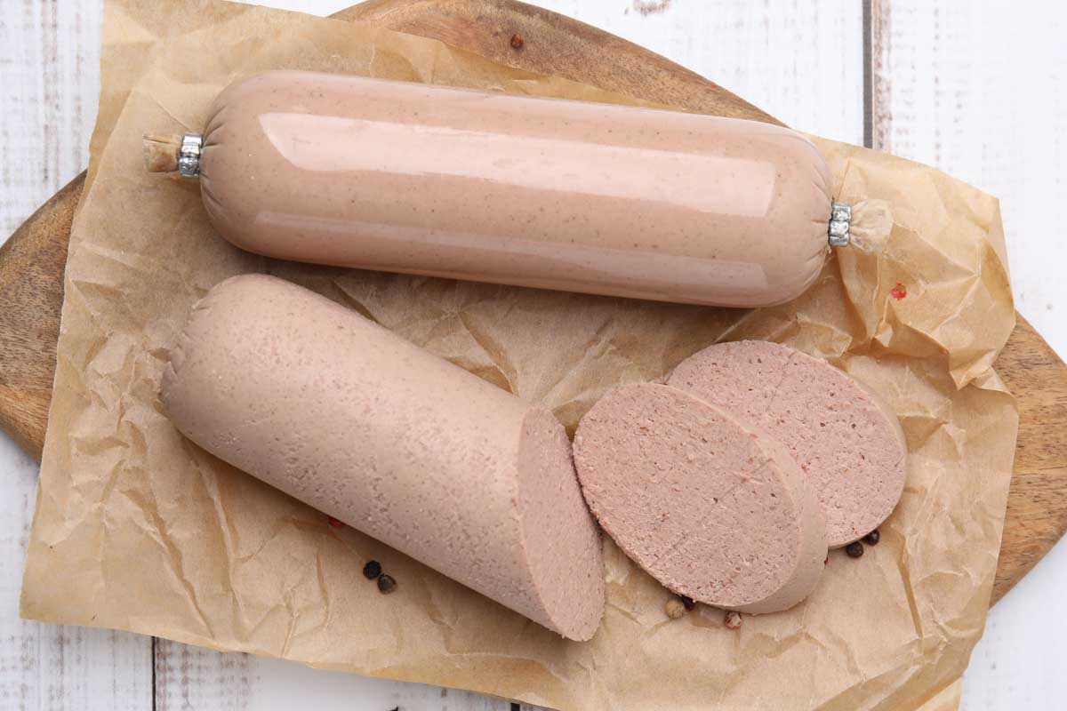 Whole and sliced liverwurst on a cutting board.