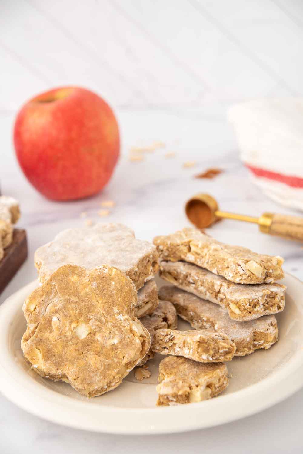 Homemade apple cinnamon dog treats on a plate and an apple behind it.
