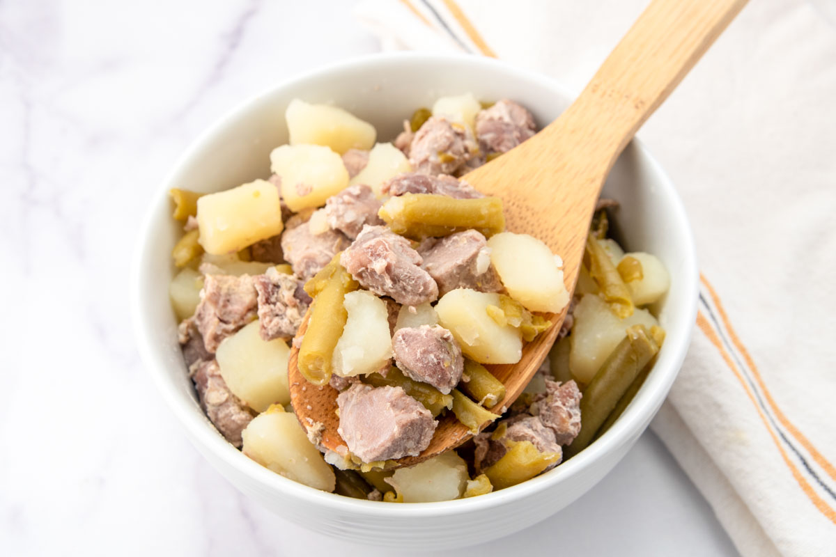 Homemade rabbit dog food with potatoes and green beans on a wooden spoon and bowl.