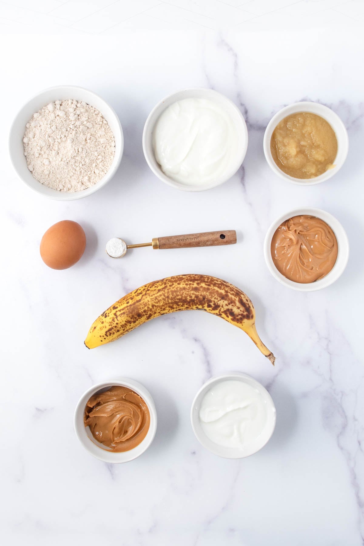 Homemade peanut butter banana pupcakes ingredients on a marble surface.