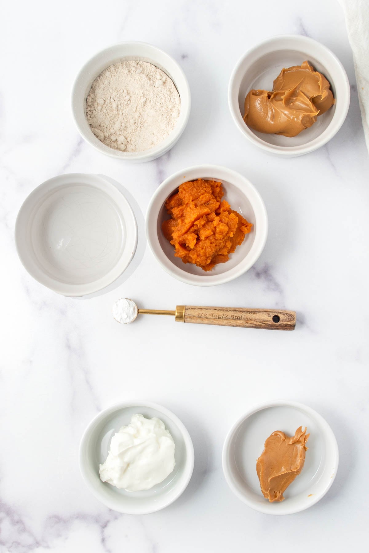 Mug cake for dogs ingredients in bowls on a marble surface.