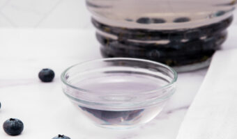 Blueberry water for dogs in a small glass bowl and glass pitcher.