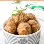 Homemade chicken meatballs for dogs in a dog bowl with a fresh rosemary sprig on top.