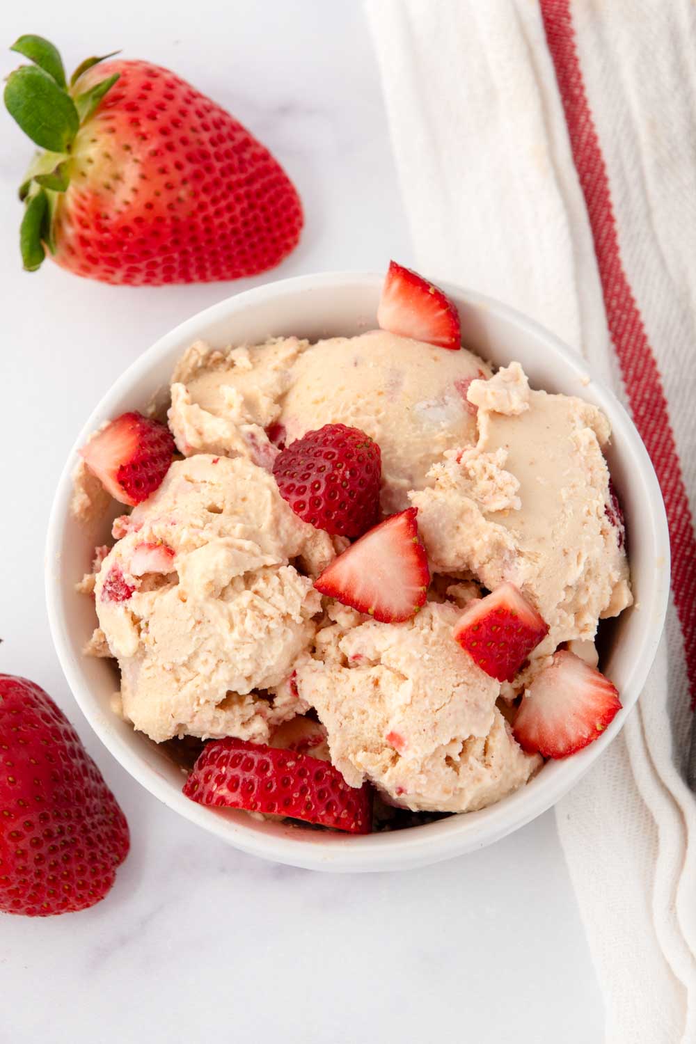 A bowl of strawberry cottage cheese ice cream for dogs and fresh strawberries.