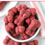 Homemade bone-shaped beet dog treats in and beside a small bowl.