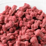 Homemade bone-shaped beet dog treats piled on a plate.