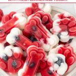 Homemade frozen berry dog treats in bone and paw shapes piled on a plate.