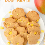 Paw-shaped homemade mango dog treats on a plate and a mango next to it.