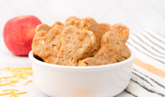 Homemade apple cheddar dog treats in a bowl and an apple behind it.