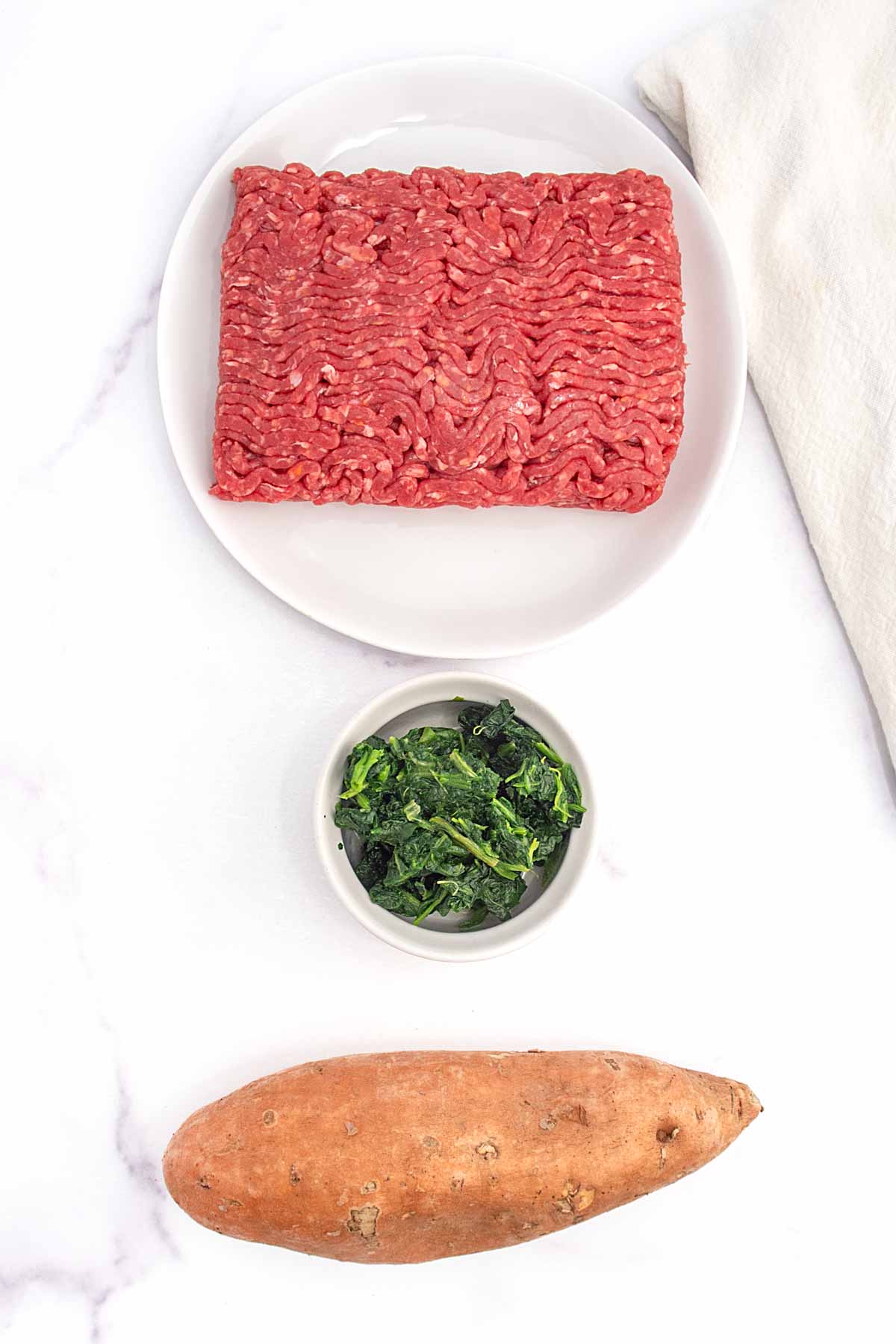 Homemade beef and sweet potato dog food ingredients on a marble surface.