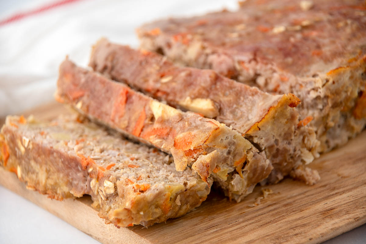 Homemade pork and apple meatloaf for dogs on a wood cutting board.