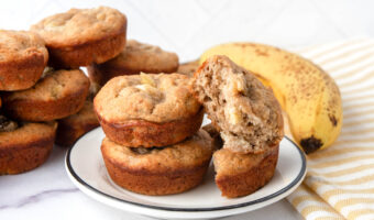 Banana muffins for dogs in a stack and on a plate, a banana, and a kitchen towel.