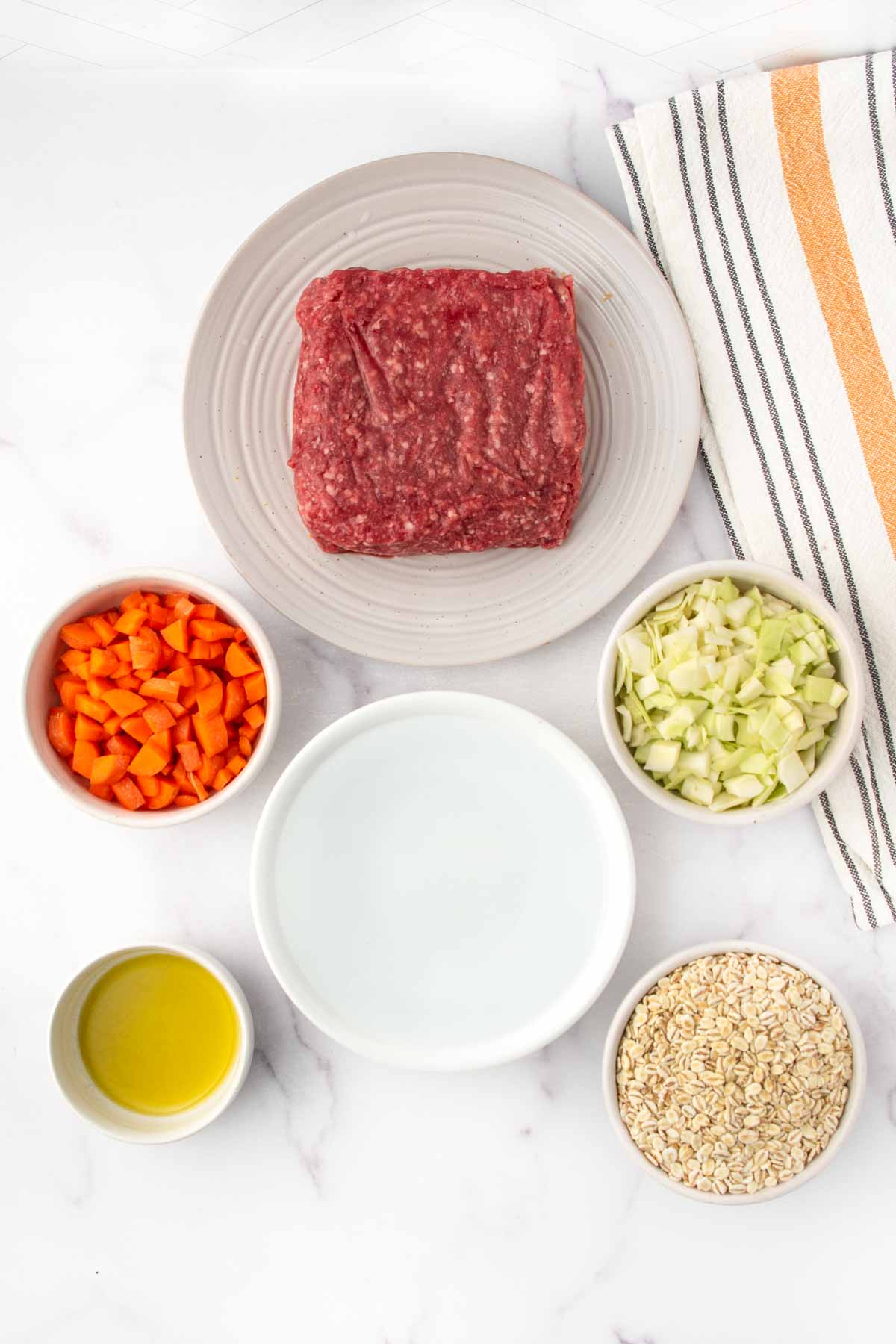Homemade ground lamb and barley dog food ingredients on a marble surface.