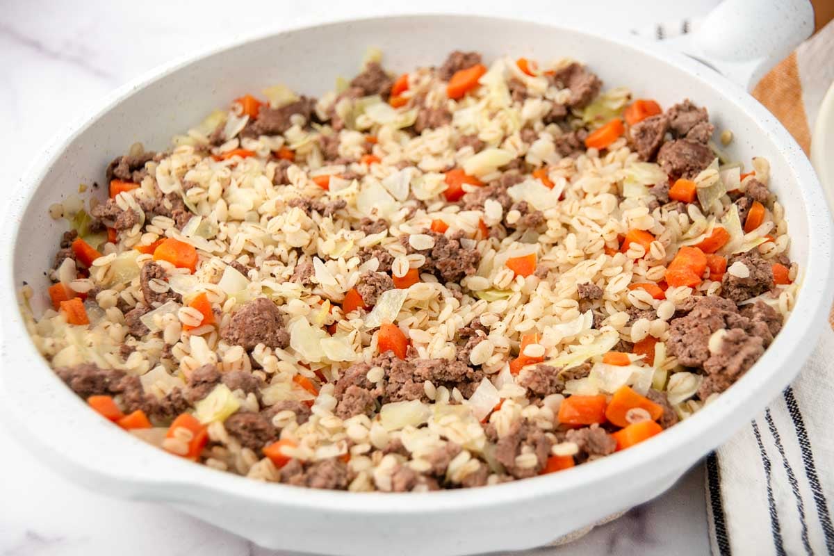 Homemade ground lamb and barley dog food in a skillet and a kitchen towel next to it.