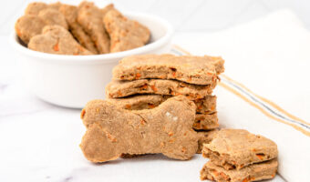 Homemade carrot cake dog treats in a bowl and stacked in front of it.