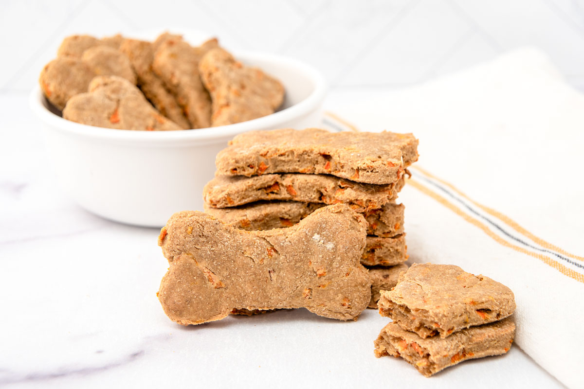 Homemade carrot cake dog treats in a stack and bowl on a marble surface.