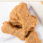 Homemade bone-shaped carrot cake dog treats in a stack on a marble surface.