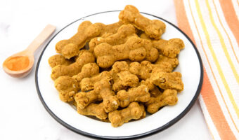 Homemade turmeric dog treats, turmeric in a wooden spoon, and a kitchen towel.