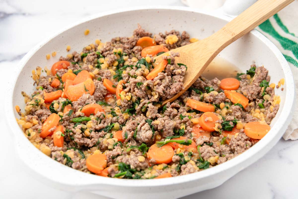 Ground beef, lentils, sliced carrots, and spinach in a skillet.