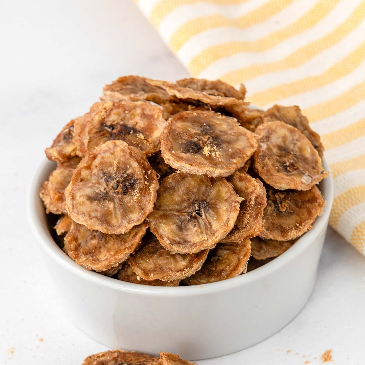 Homemade ginger flavored dehydrated banana chips for dogs in a small bowl.