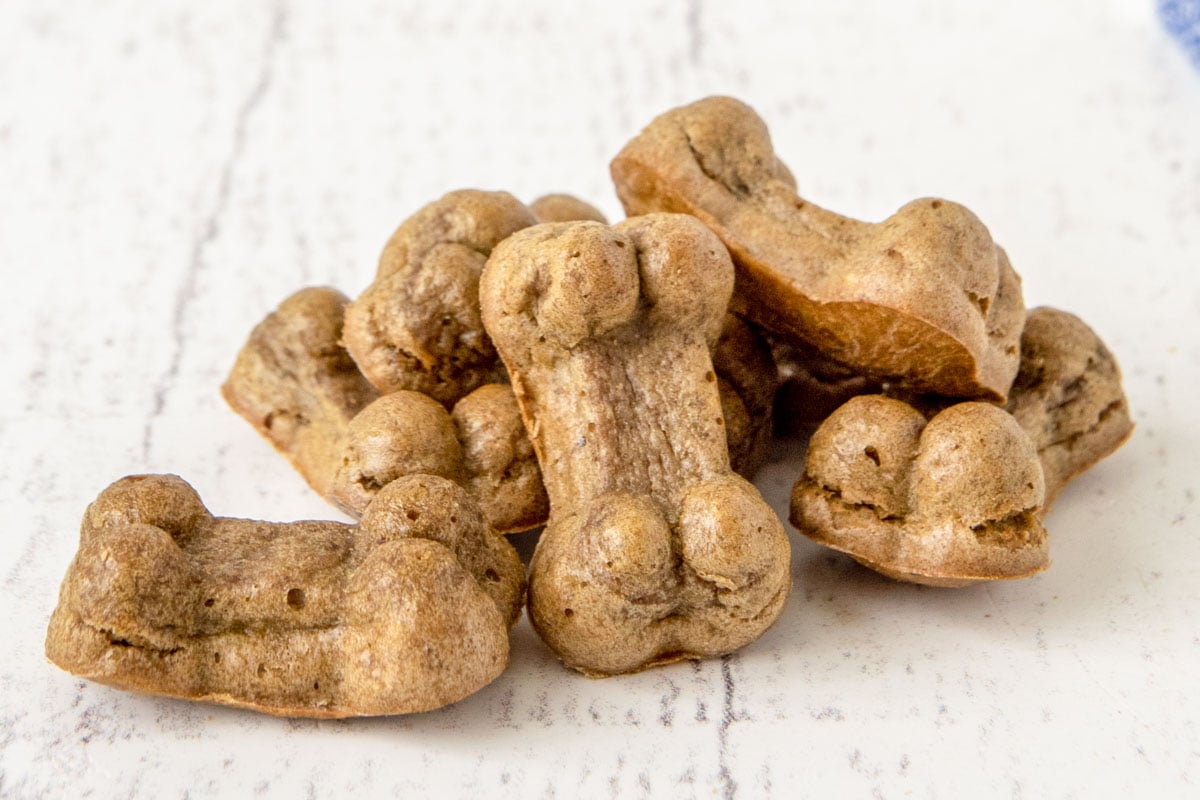 Homemade bone-shaped liver dog treats in a pile on a wood surface.