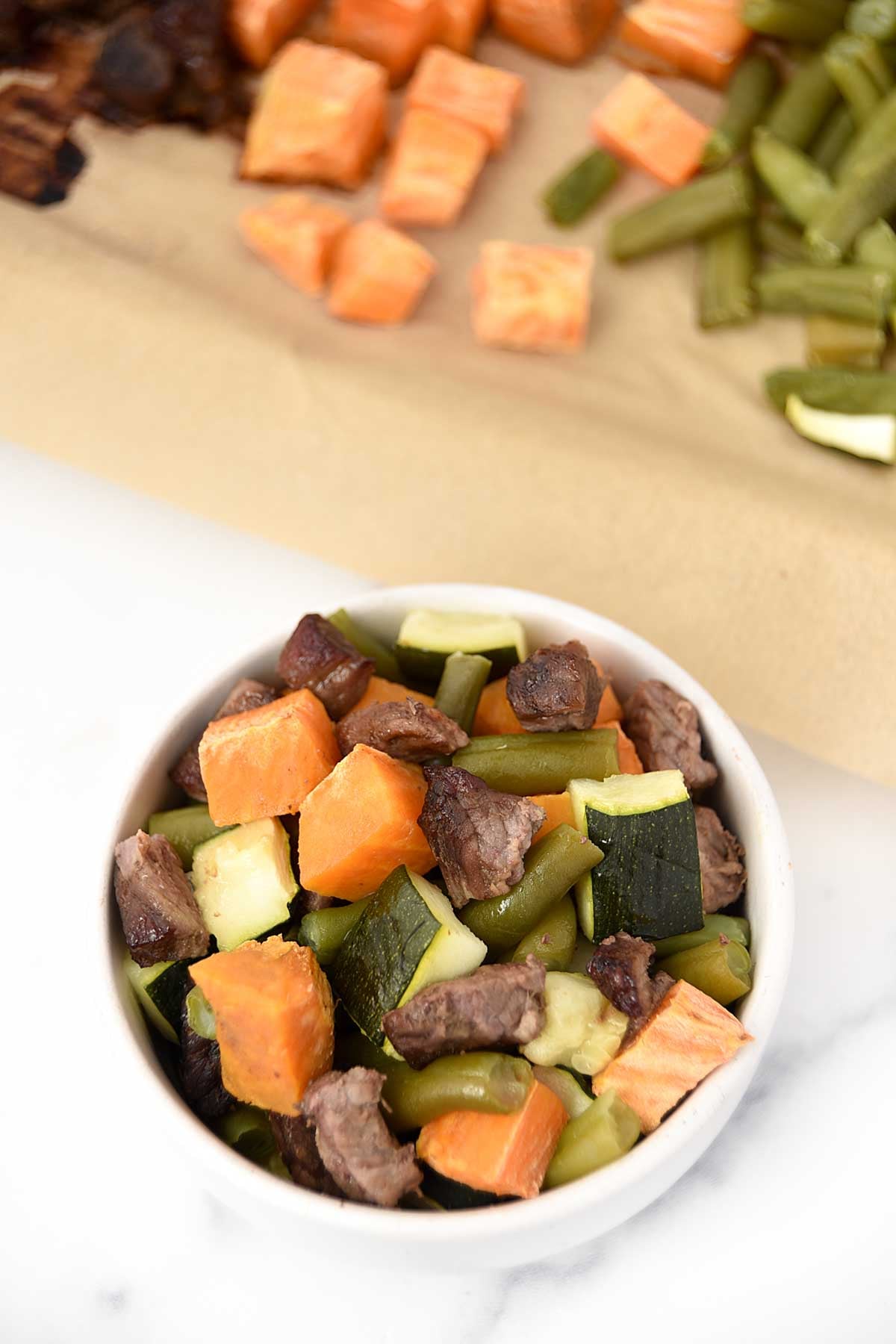 Homemade beef and vegetable dog food in a small bowl and on a sheet pan.