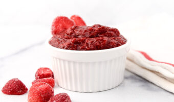 Homemade strawberry jam for dogs in a small bowl and strawberries next to it.