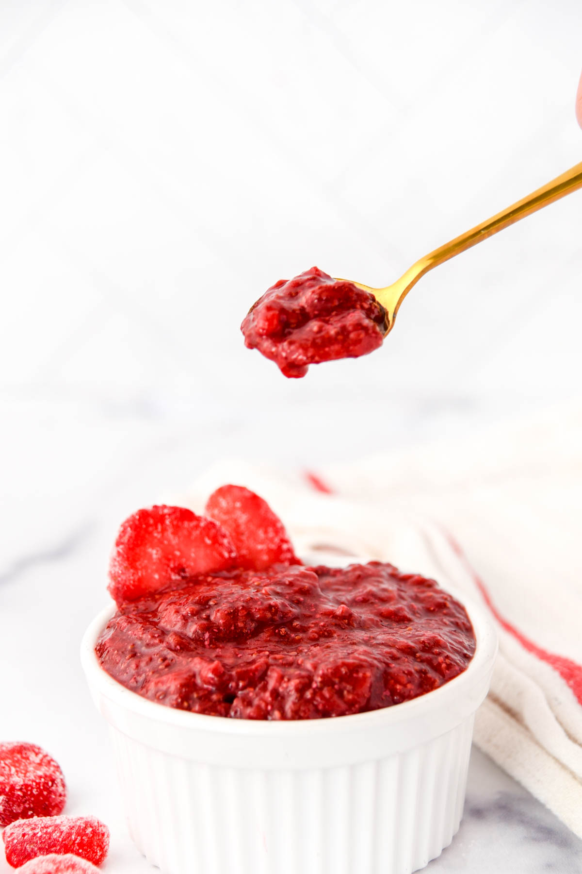 Strawberry jam on a small spoon over the jam in a ramekin.