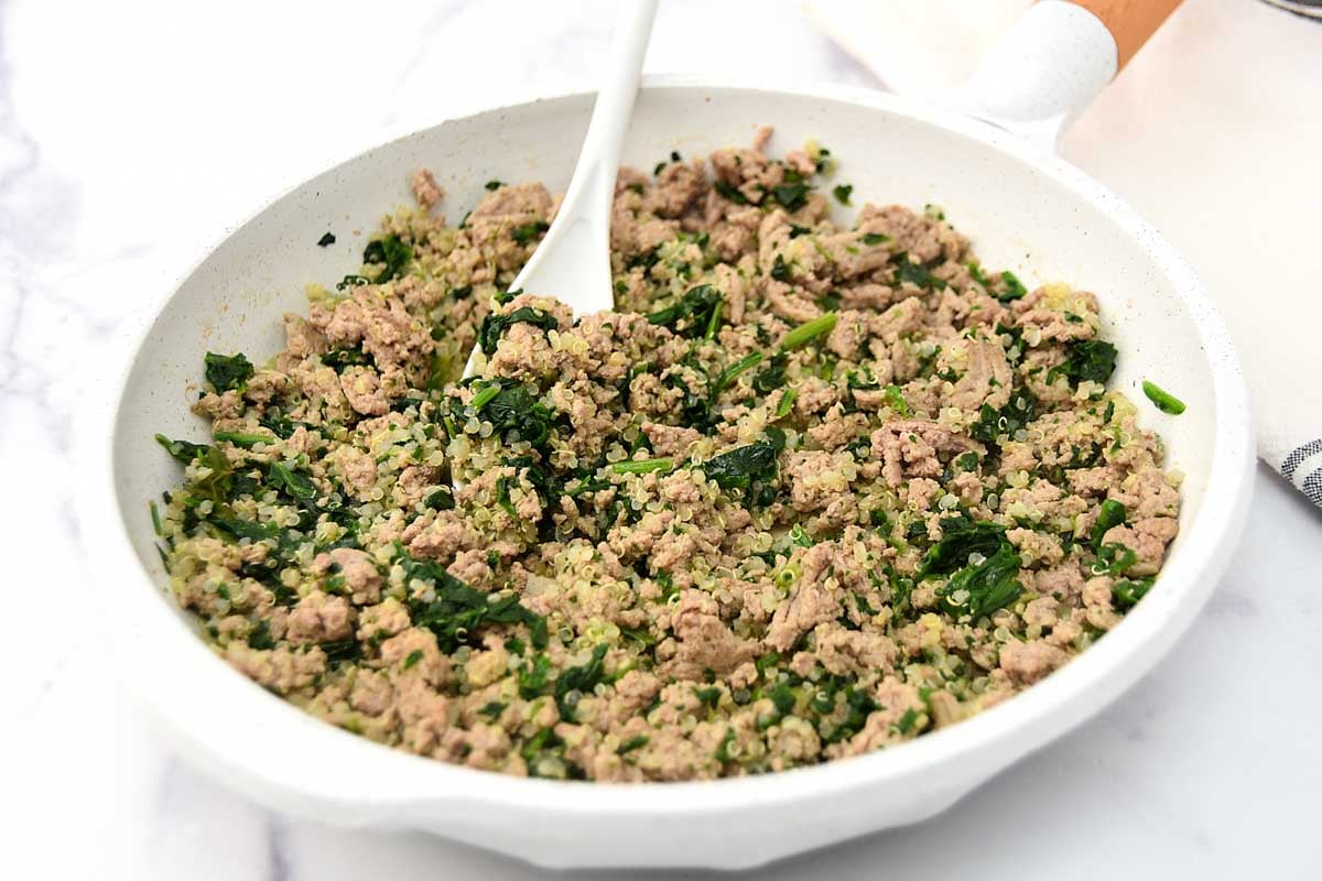 Turkey, spinach, and quinoa dog food in a skillet on a marble surface.