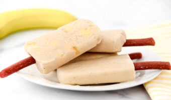 A pile of homemade banana popsicles for dogs on a plate and a banana behind it.