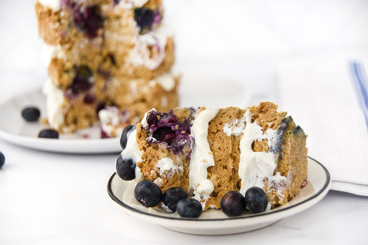 A slice of blueberry cake and fresh blueberries on a small plate.