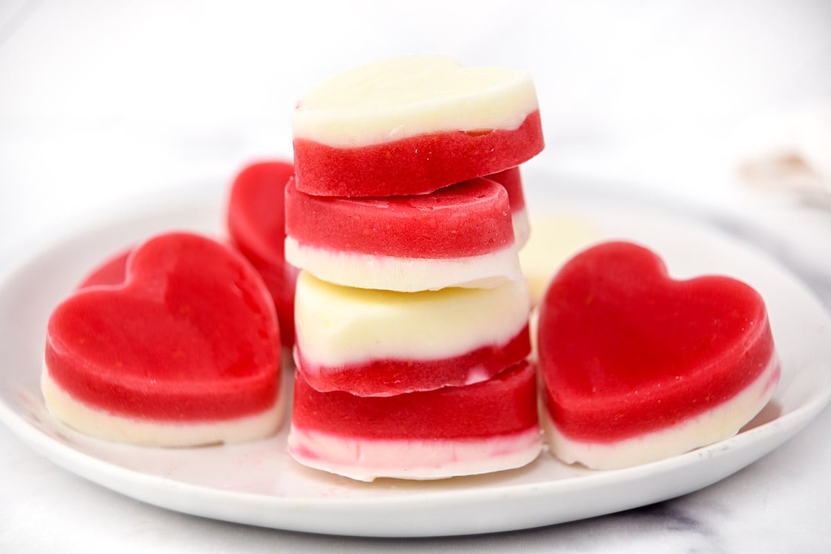 Heart-shaped frozen raspberry dog treats stacked and scattered on a plate.