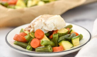 Sheet pan baked white fish over carrots, green beans, and zucchini on a plate.