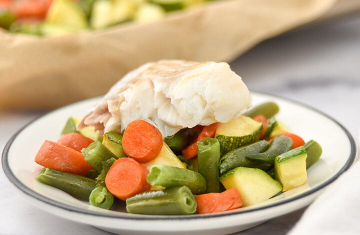 Sheet pan baked white fish over carrots, green beans, and zucchini on a plate.